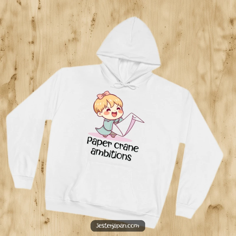 Funny Kawaii hoodie showing a character cheerfully grappling with an impossibly large origami crane, embodying the humor of grand creative attempts.